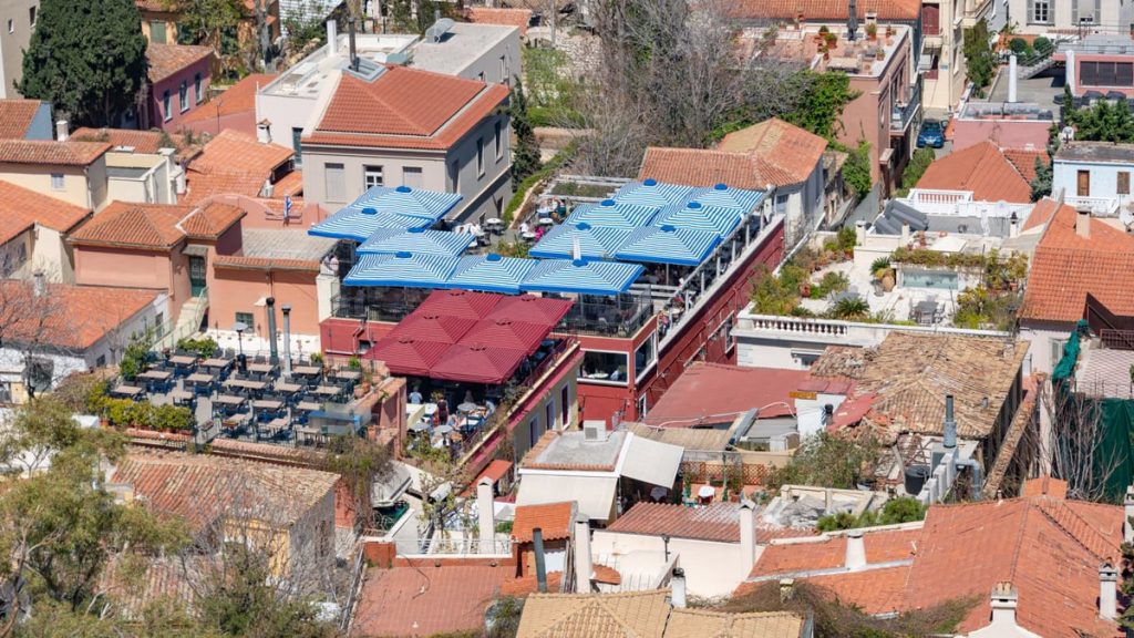 Aerial capture of a sunlit town with traditional rooftops and vibrant umbrellas creating an inviting outdoor space.