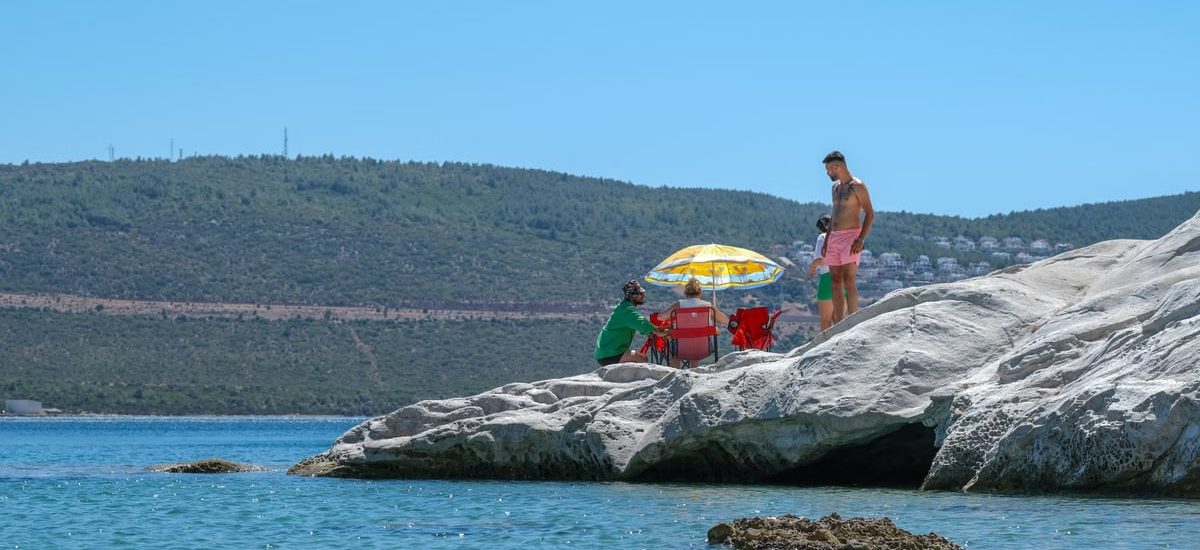A group of people relaxing on rocky shore under a colorful umbrella on a sunny day
