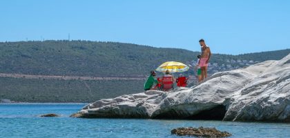 A group of people relaxing on rocky shore under a colorful umbrella on a sunny day
