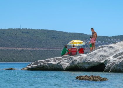 A group of people relaxing on rocky shore under a colorful umbrella on a sunny day