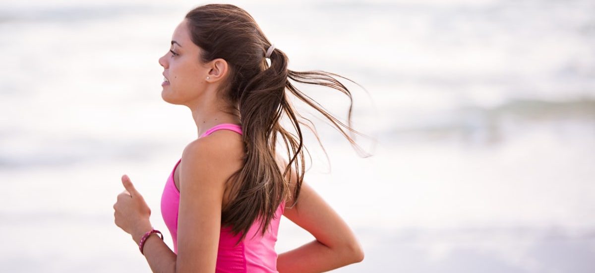 Side view of a young woman jogging on a beach wearing pink active wear.