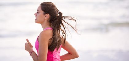 Side view of a young woman jogging on a beach wearing pink active wear.