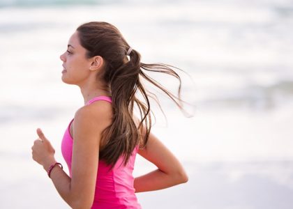 Side view of a young woman jogging on a beach wearing pink active wear.